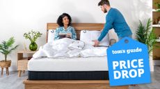 A couple laugh while the woman lies on the Panda Hybrid Bamboo Mattress Pro, set on a wooden bed frame, with a blue price drop sales badge overlaid in the bottom right corner