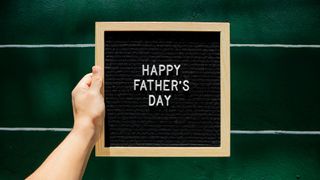 Hand holding Father's Day sign with green tiled background